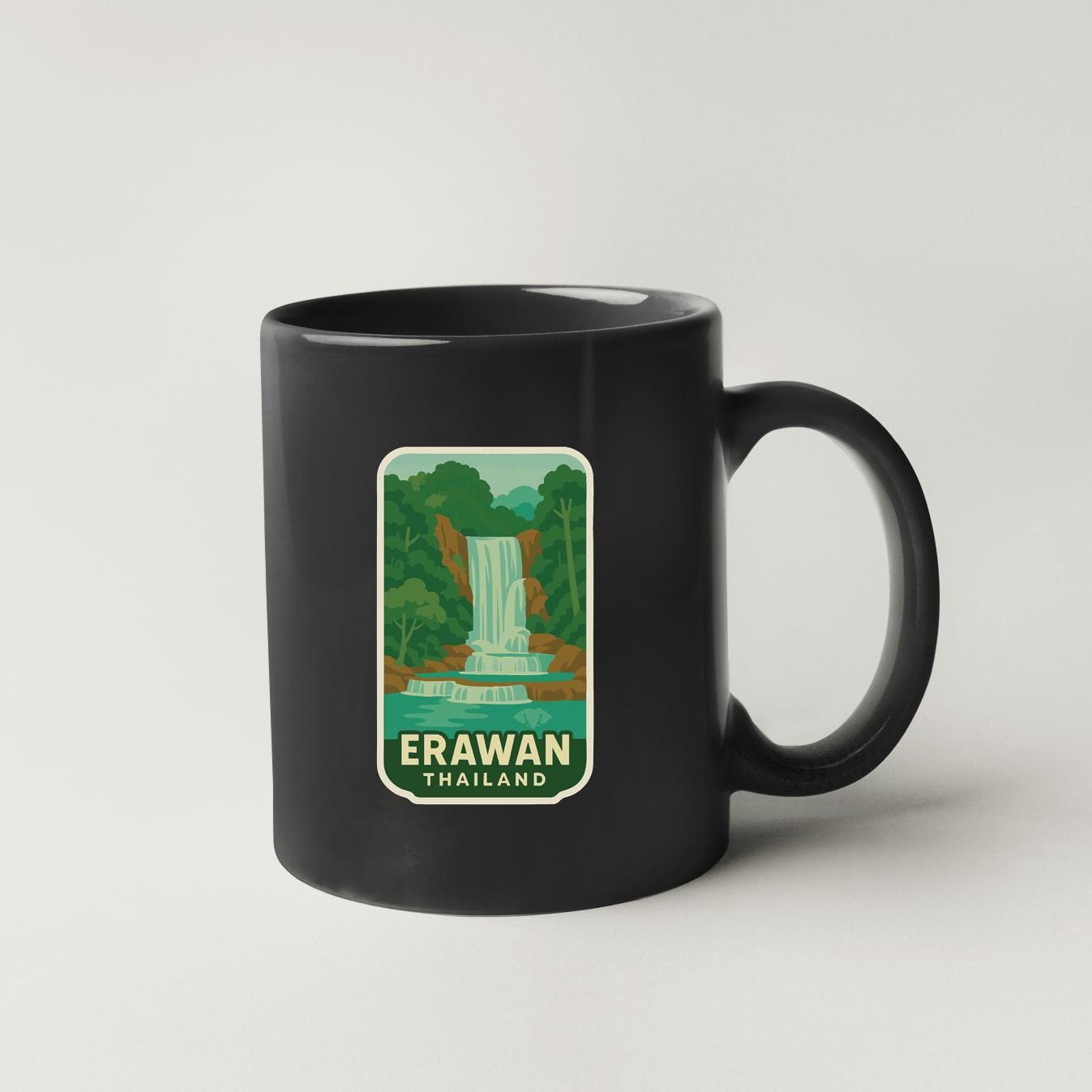 A black coffee mug with a sticker depicting a waterfall in a tropical setting.