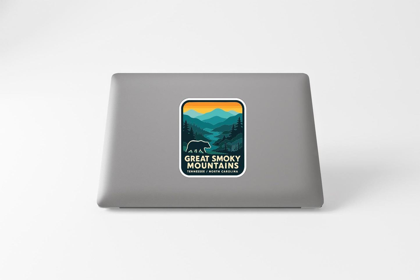 A sticker on the back of a laptop, depicting a scenic mountain landscape with a bear in the foreground.