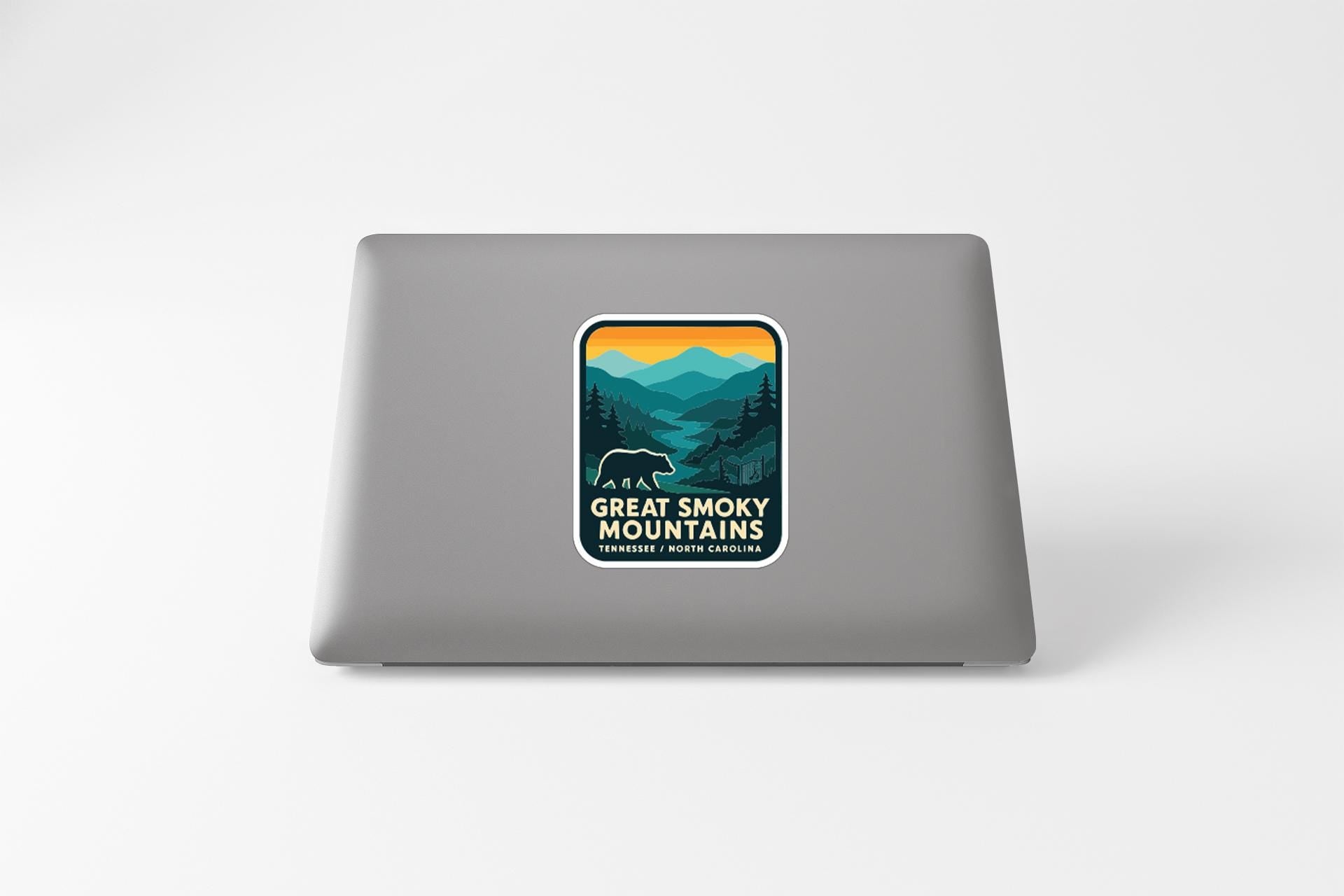A sticker on the back of a laptop, depicting a scenic mountain landscape with a bear in the foreground.