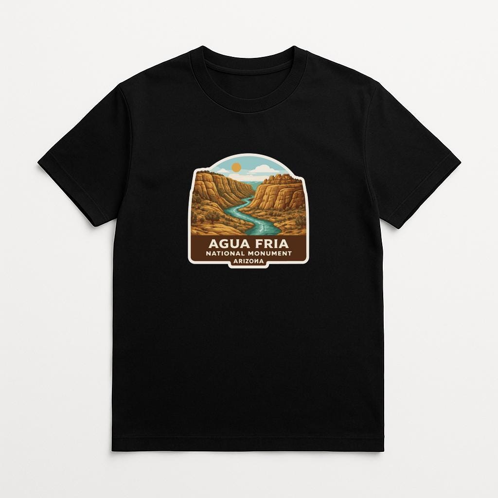 A black t-shirt with a graphic design depicting the scenic landscape of the Agua Fría National Monument in Arizona.