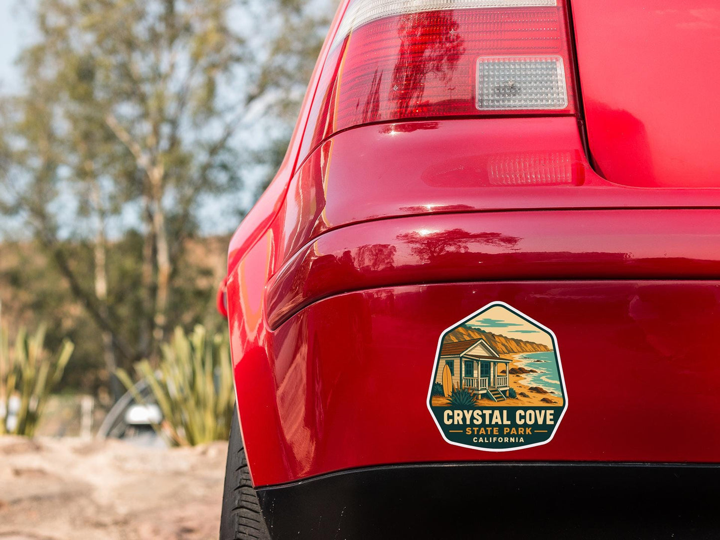 the rear end of a red car with a sticker on the back window that says "CRYSTAL COVE STATE PARK CALIFORNIA".