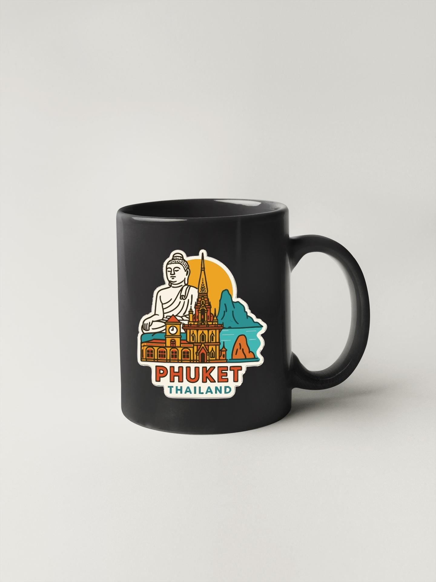 A black coffee mug with a colorful illustration of the city of Phuket, Thailand, featuring a Buddha statue and various landmarks.