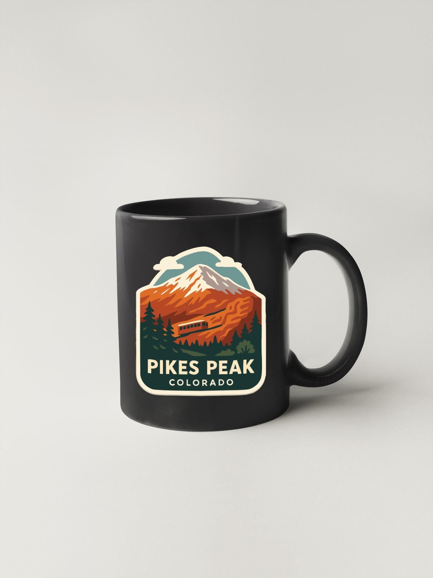 A black coffee mug with a mountain landscape and text that says "Pikes Peak, Colorado" printed on it.