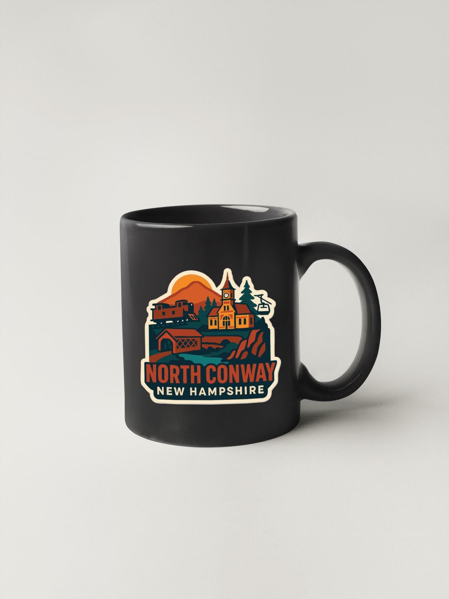 A black coffee mug with a colorful graphic design depicting a scenic landscape with a church, buildings, and a sunset.