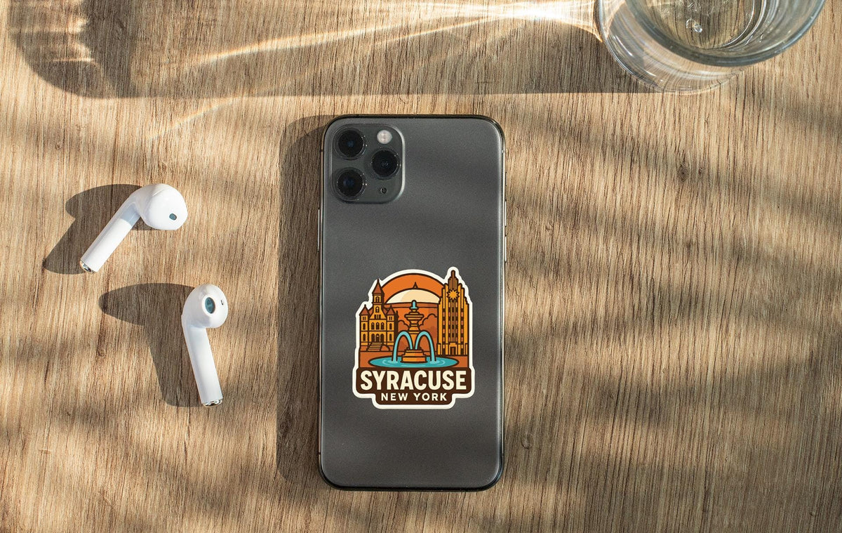a smartphone with a sticker of Niagara Falls on it, along with a pair of white earbuds and a glass of water on a wooden surface.