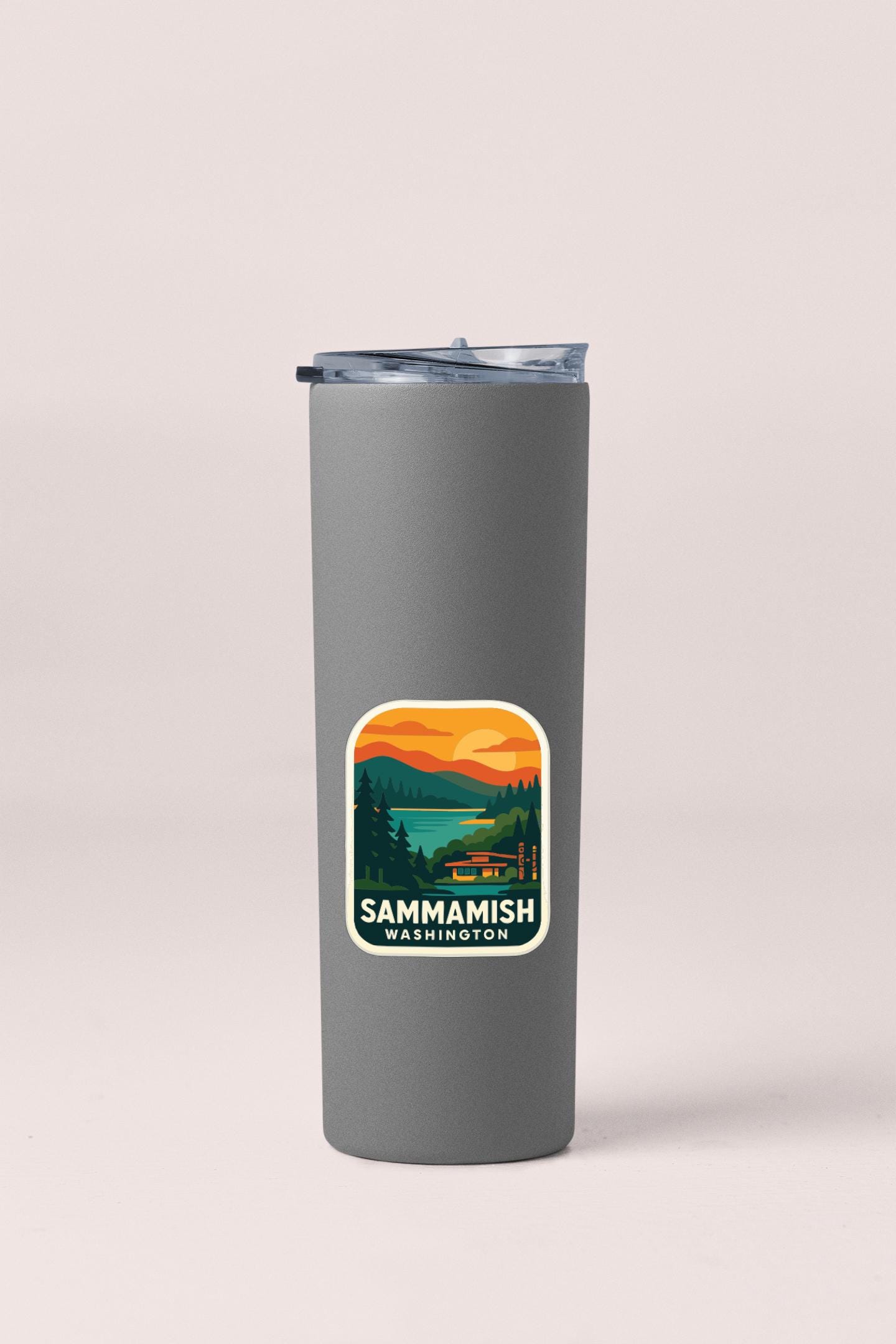 A gray insulated tumbler with a sticker on it, featuring a scenic landscape with mountains, trees, and a lake.