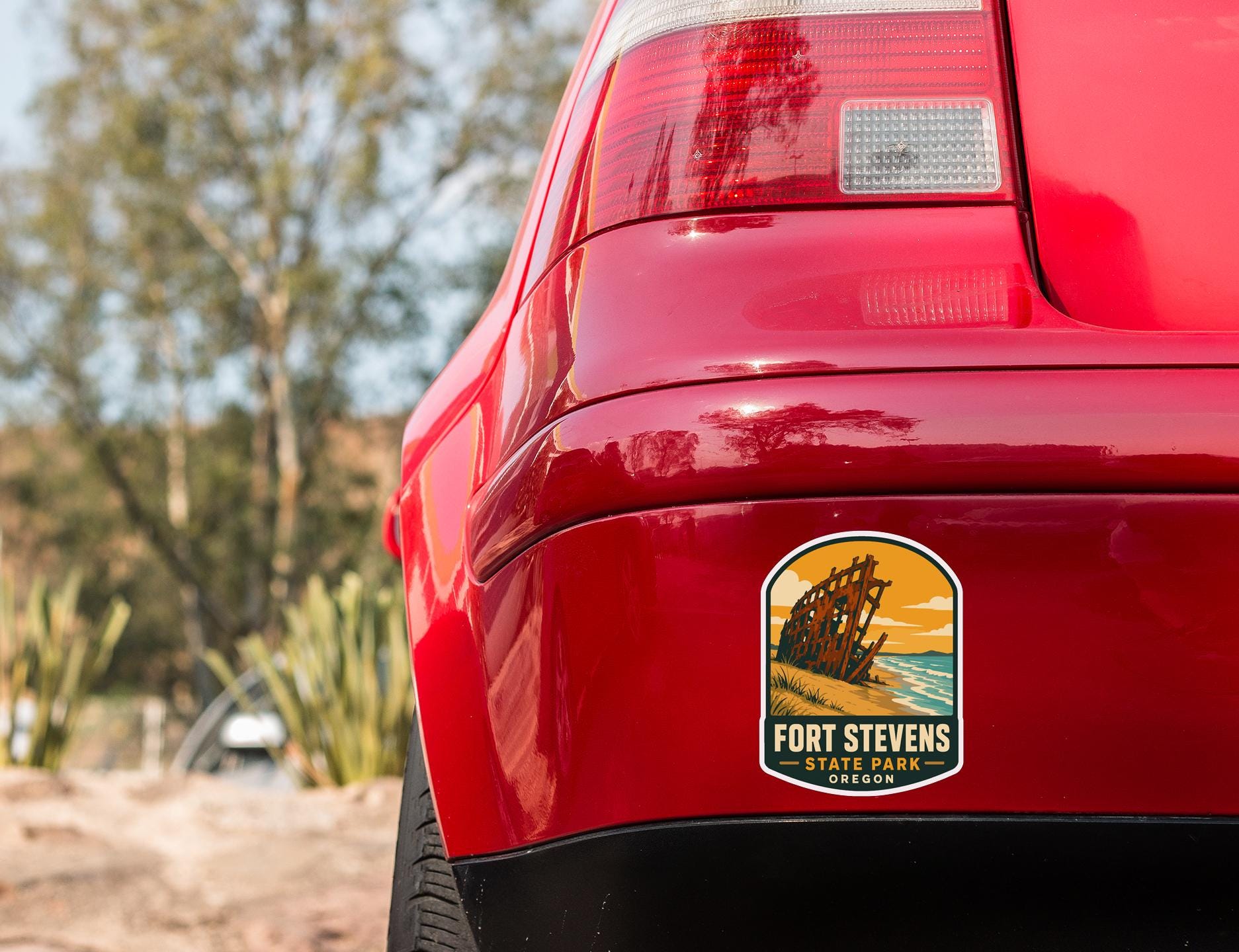 the rear end of a red car with a sticker on the back window that reads "Fort Stevens State Park, Oregon".