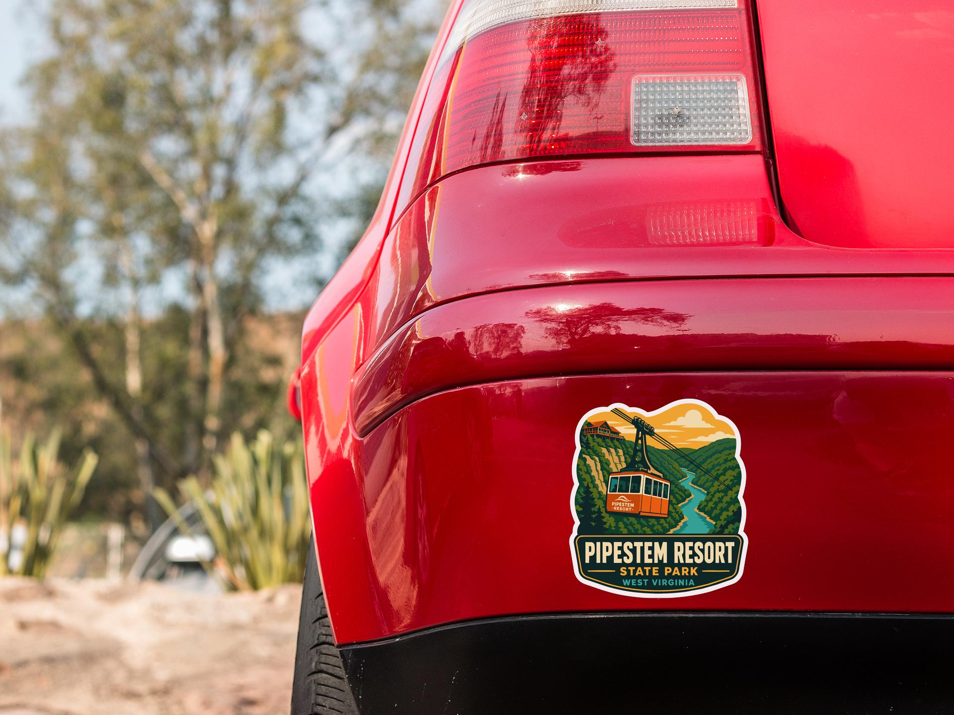 the rear end of a red car with a sticker on it, featuring a scenic landscape with a river and mountains.