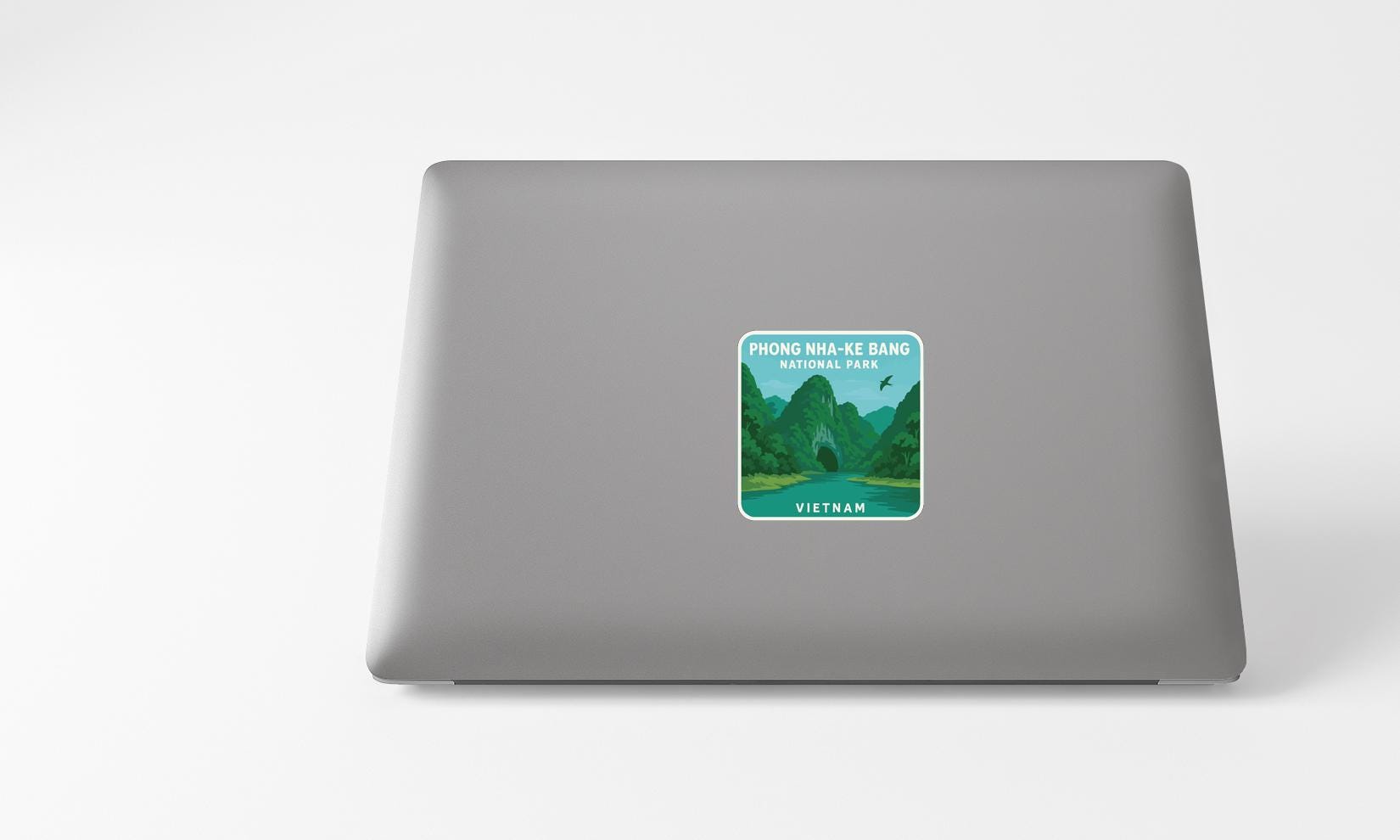 A sticker depicting a scenic landscape with mountains and a river, placed on the back of a laptop computer.