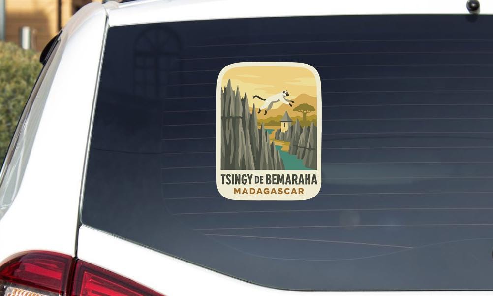 A sticker on the rear window of a car, depicting a scenic landscape with mountains, a river, and a cat.