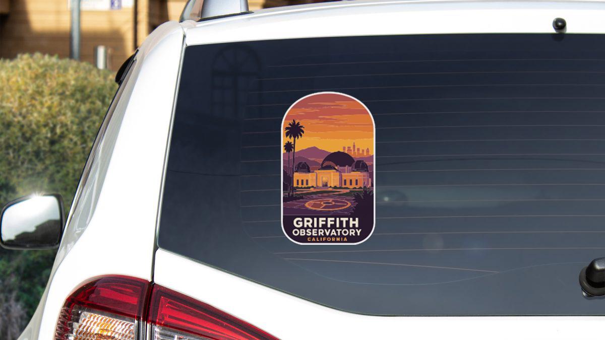 A sticker on the rear window of a white car, depicting a scenic view of Griffith Observatory in California.