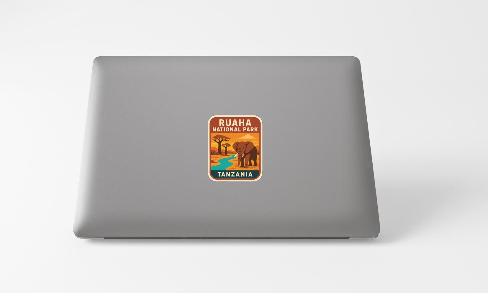 a sticker with an illustration of an elephant and the text "RUHA PARK TANZANIA" on a grey laptop.