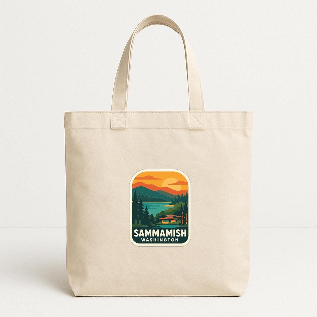 A beige tote bag with a printed sticker depicting a scenic landscape with mountains, trees, and a sunset over a body of water.