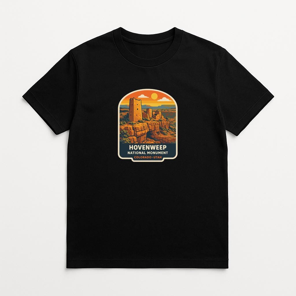 A black t-shirt with a graphic design depicting a desert landscape with a tower in the center, surrounded by a colorful sky.