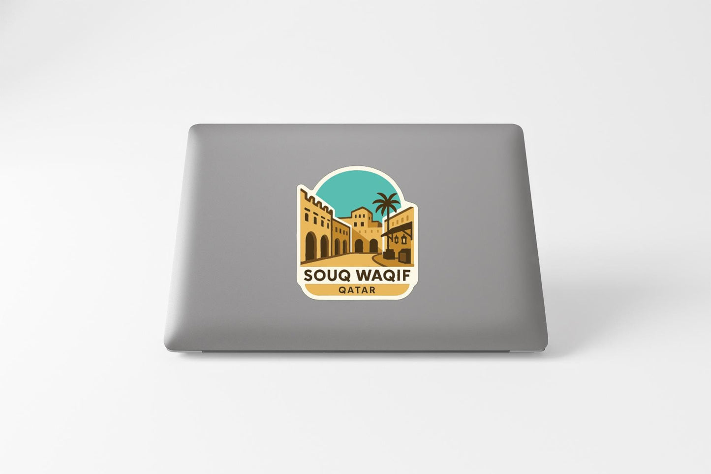 a sticker or decal on the back of a laptop, depicting a cityscape with a palm tree and buildings, along with the text "SOUQ WAIFI QAR".