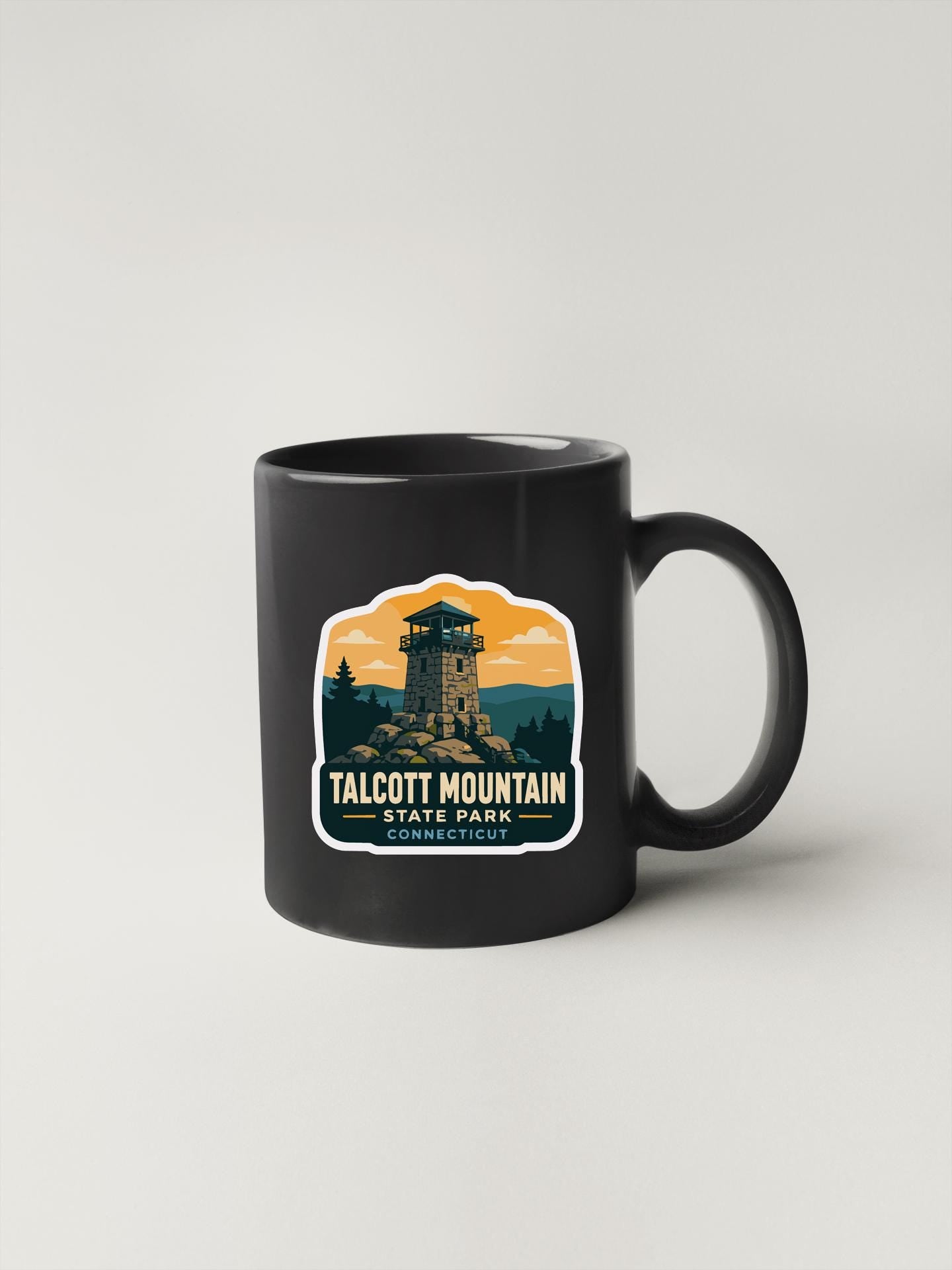 A black coffee mug with a graphic design depicting a tower and mountains, along with the text "TALCOT MOUNTAIN STATE PARK CONNECTICUT".