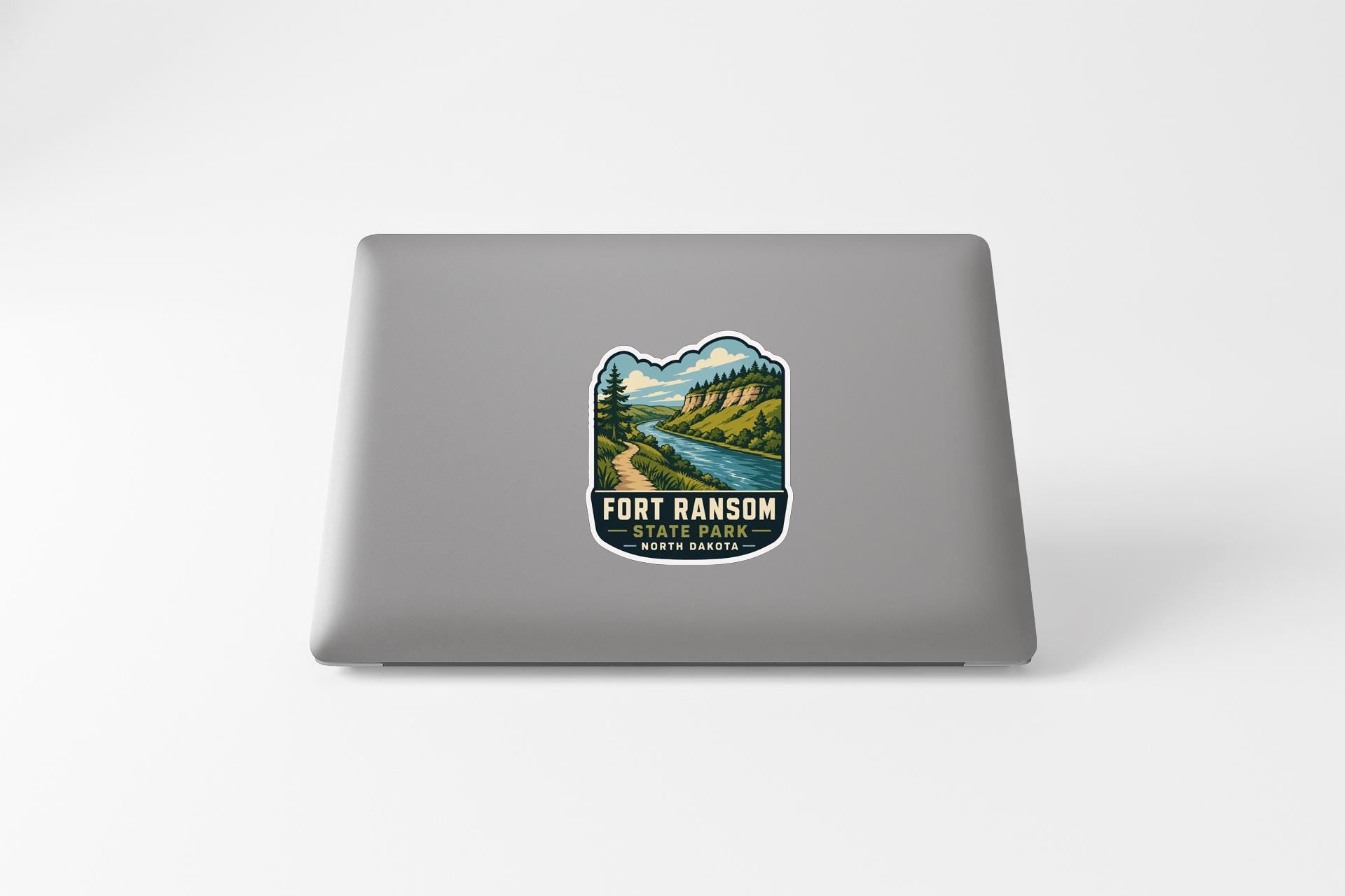 a sticker on the back of a laptop that displays a scenic landscape with a river and mountains.