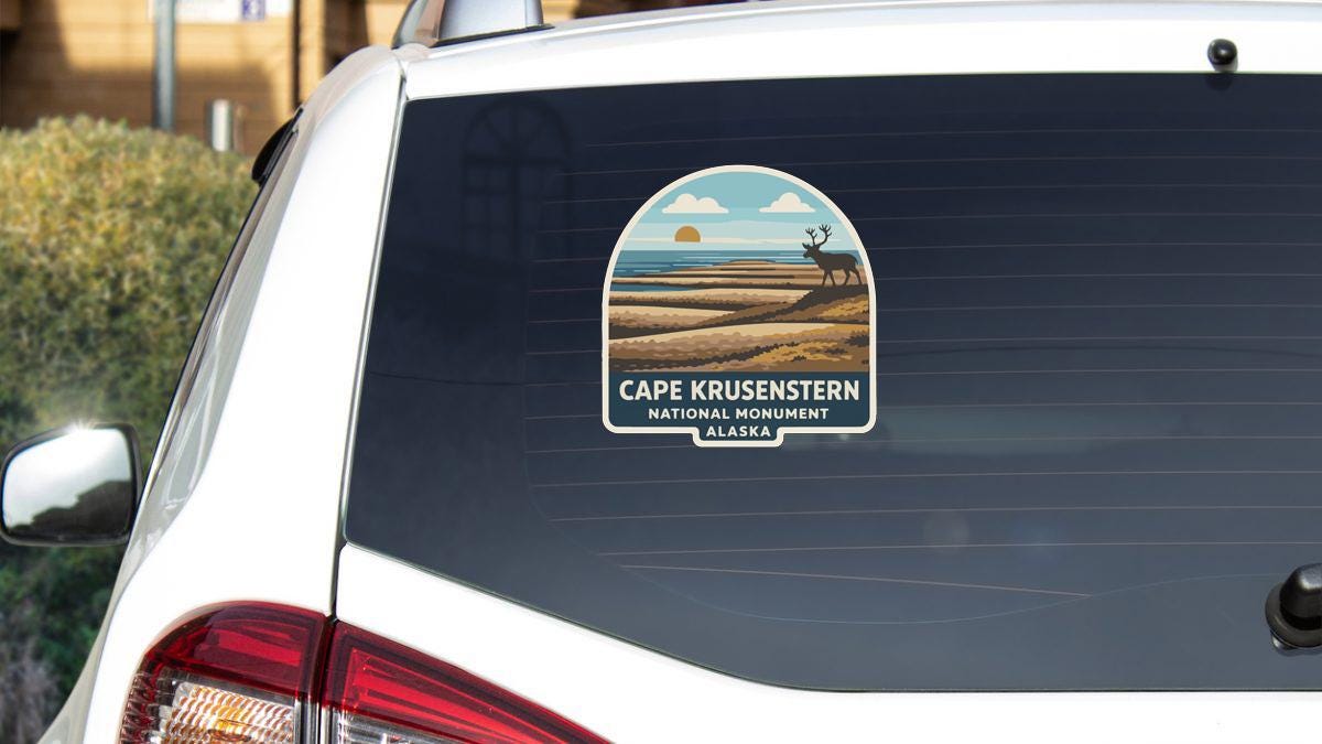a sticker on the rear window of a car, depicting a scenic landscape with a deer in the foreground and the text "CAPE KRUSENSTERN NATIONAL MONUMENT ALASKA" printed on it.