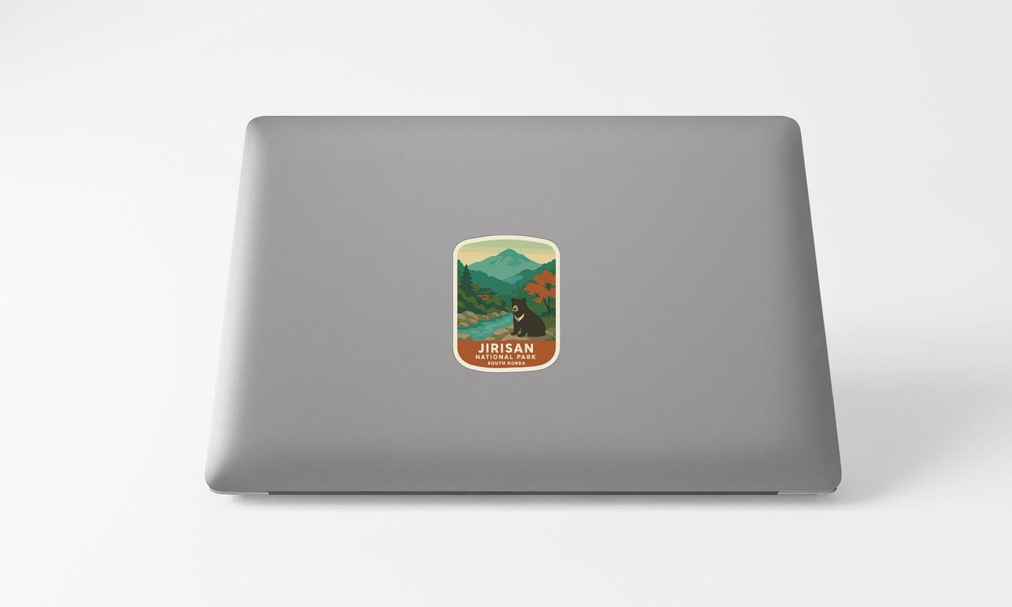 A sticker on the back of a laptop, depicting a scenic mountain landscape with a bear in the foreground.