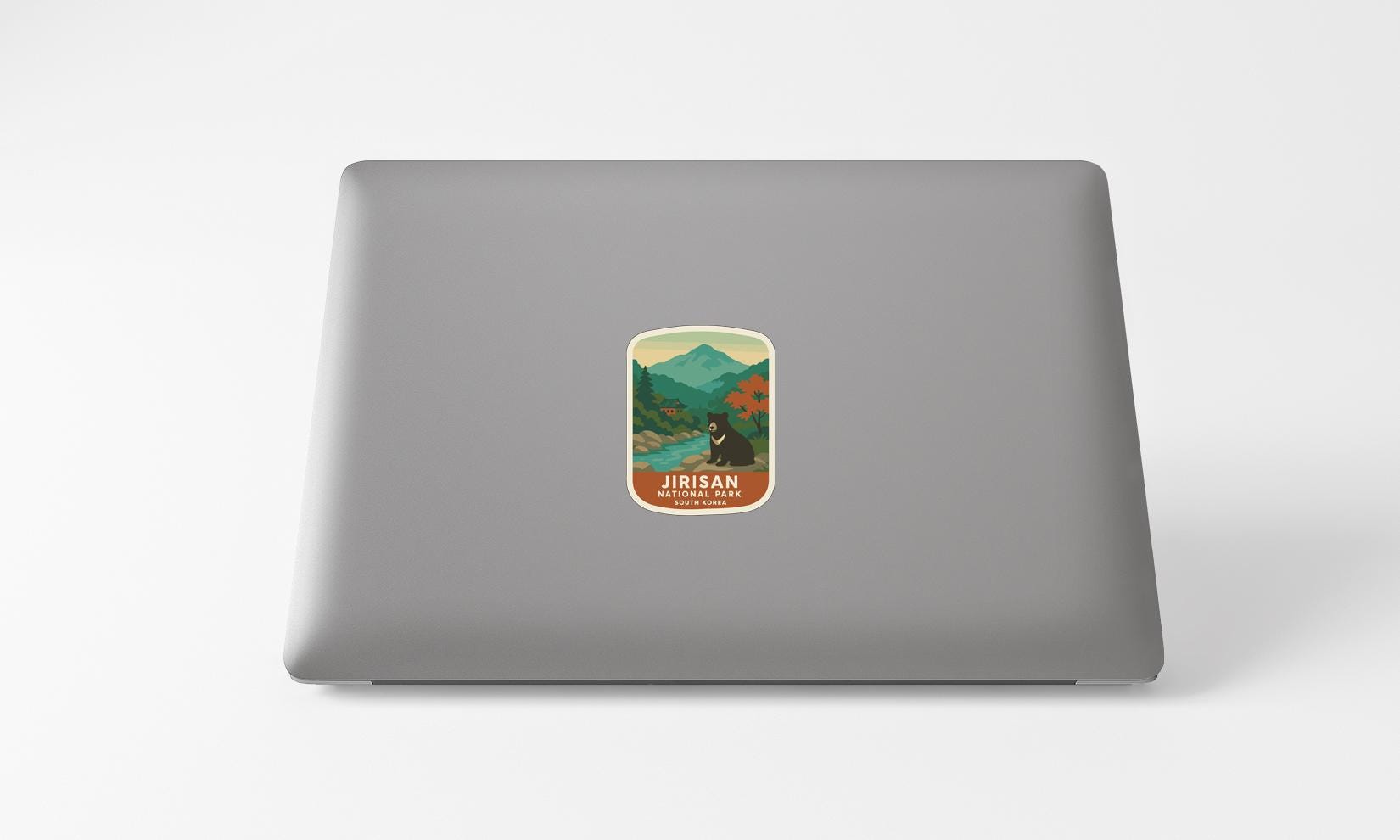 A sticker on the back of a laptop, depicting a scenic mountain landscape with a bear in the foreground.