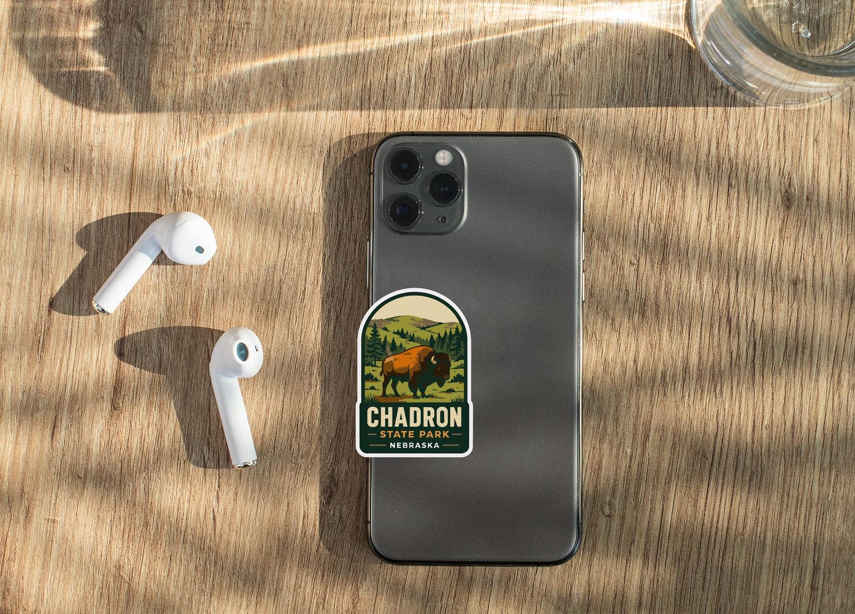 a smartphone with a sticker on it, placed on a wooden surface alongside a pair of white earbuds.