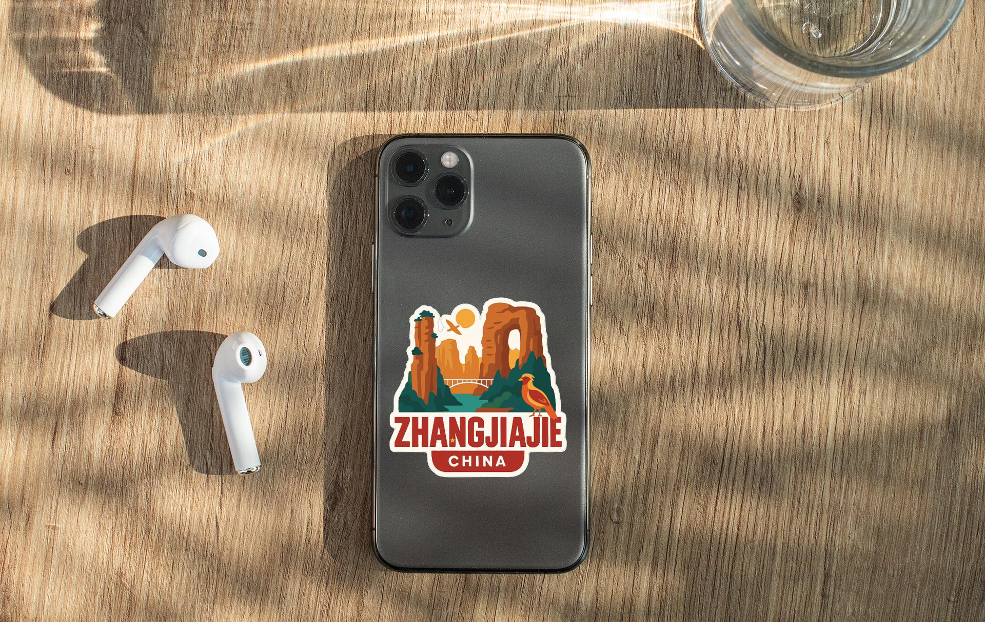 a smartphone with a sticker on the back, placed on a wooden surface alongside a pair of white earbuds and a glass of water.