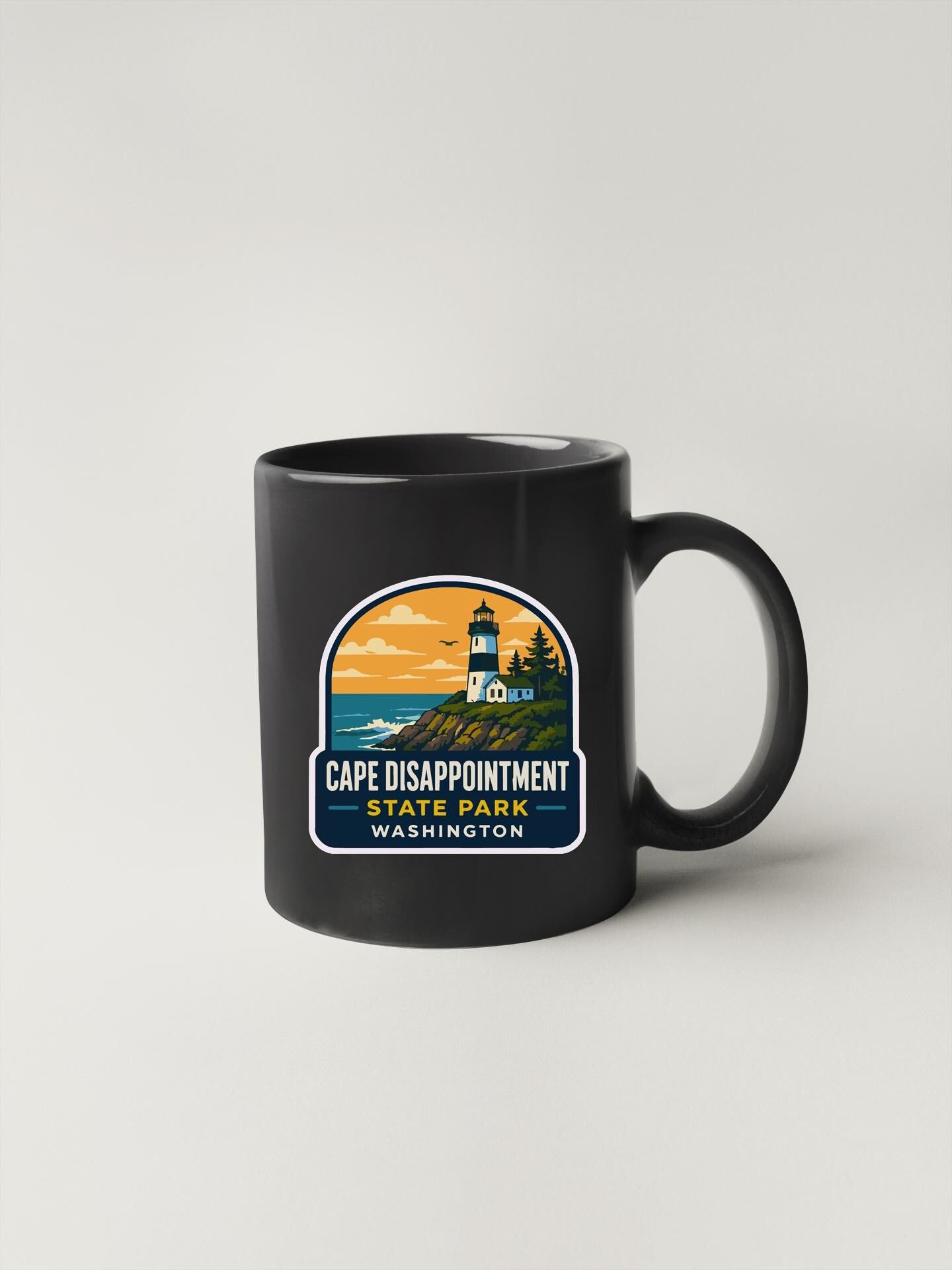 A black coffee mug with a graphic design featuring a lighthouse and the text "Cape Disappointment State Park Washington".