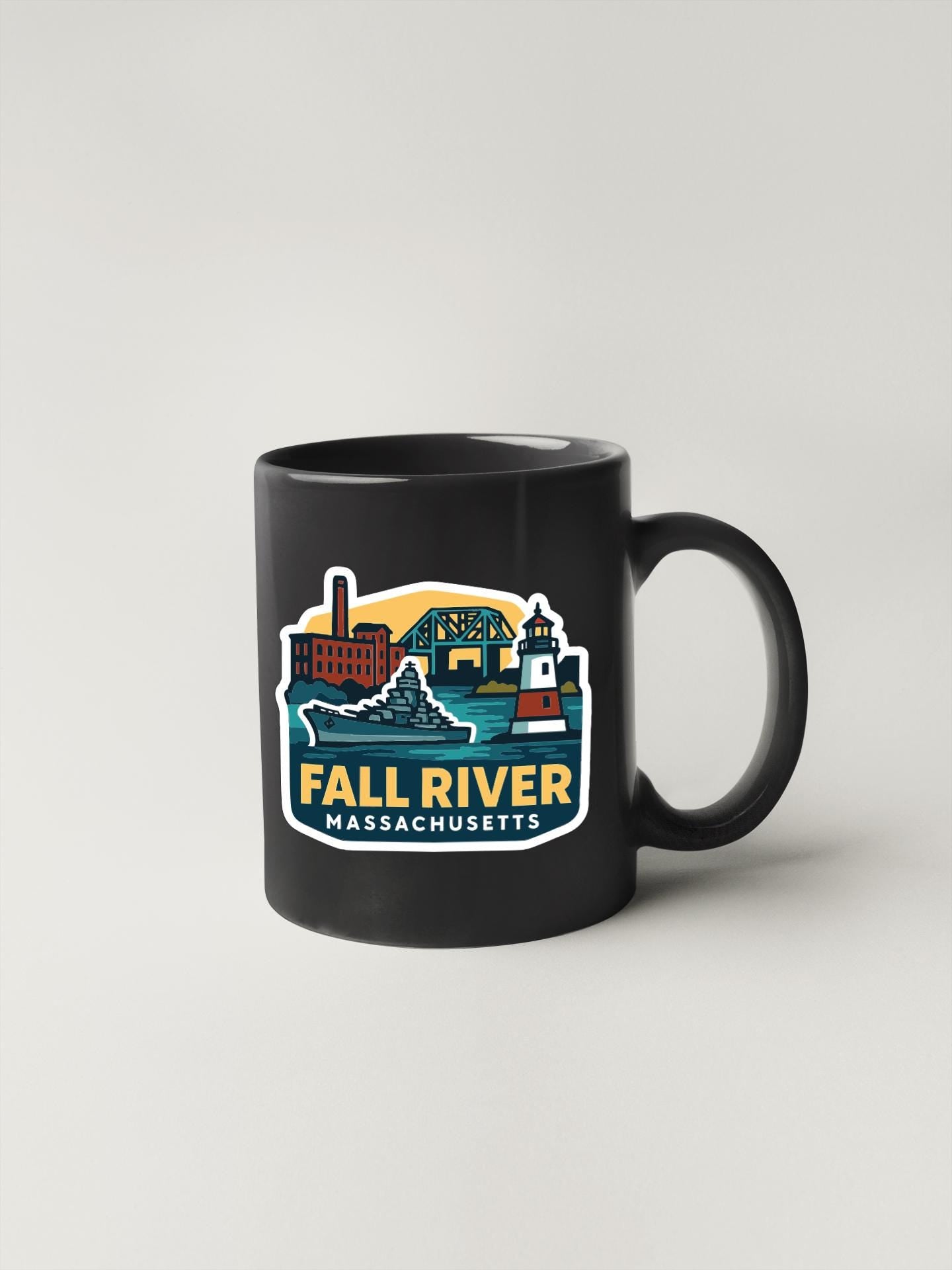 A black coffee mug with a colorful graphic depicting the Fall River, Massachusetts, featuring a lighthouse, bridge, and other landmarks.