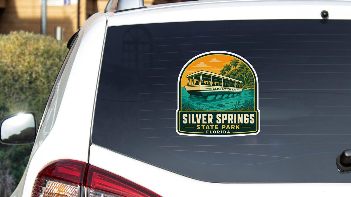 A sticker on the rear window of a white car, depicting a boat on a lake with the text "SILVER SPRINGS STATE PARK FLORIDA".