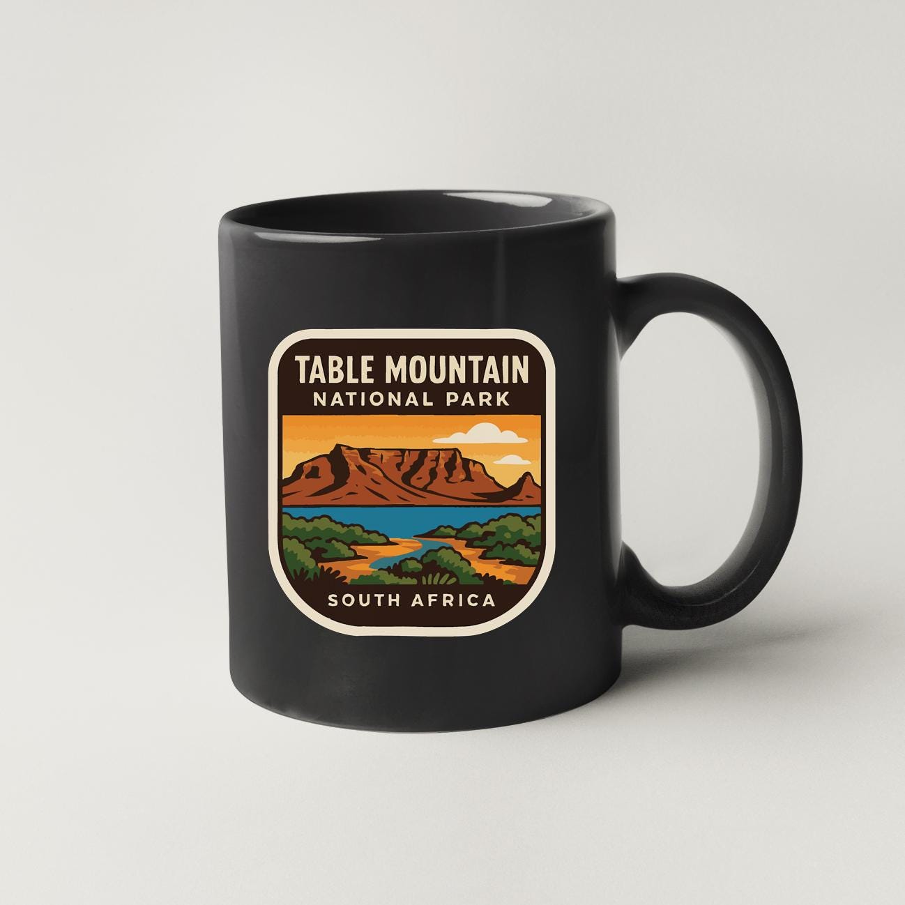 A black coffee mug with a label that says "TABLE MOUNTAIN NATIONAL PARK SOUTH AFRICA".