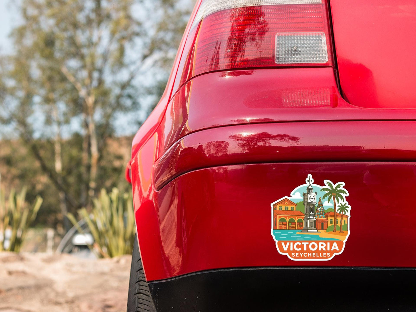 the rear end of a red car with a sticker on the trunk that features an illustration of a cityscape with a clock tower and palm trees.