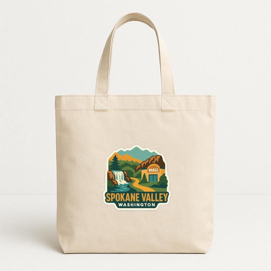 A beige tote bag with a printed design depicting a scenic landscape, including mountains, a waterfall, and a building, along with the text "SPOKANE VALLEY WASHINGTON".