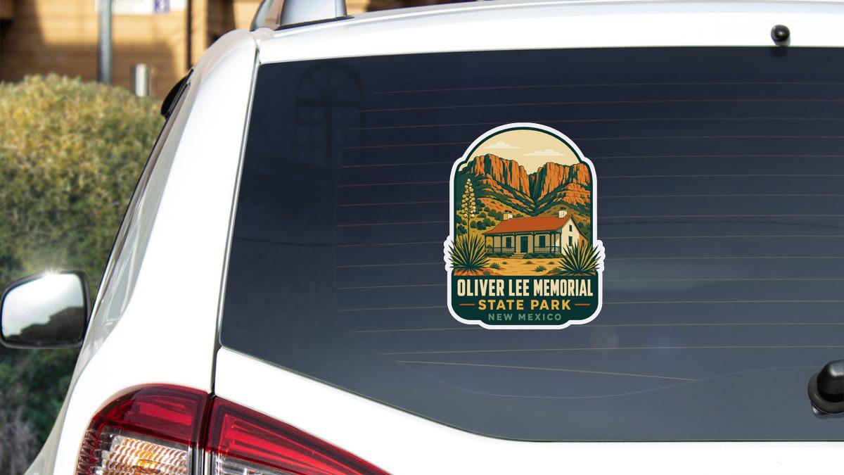 A sticker on the rear window of a white car, depicting a scenic landscape with mountains and a building, representing Oliver Lee Memorial State Park in New Mexico.