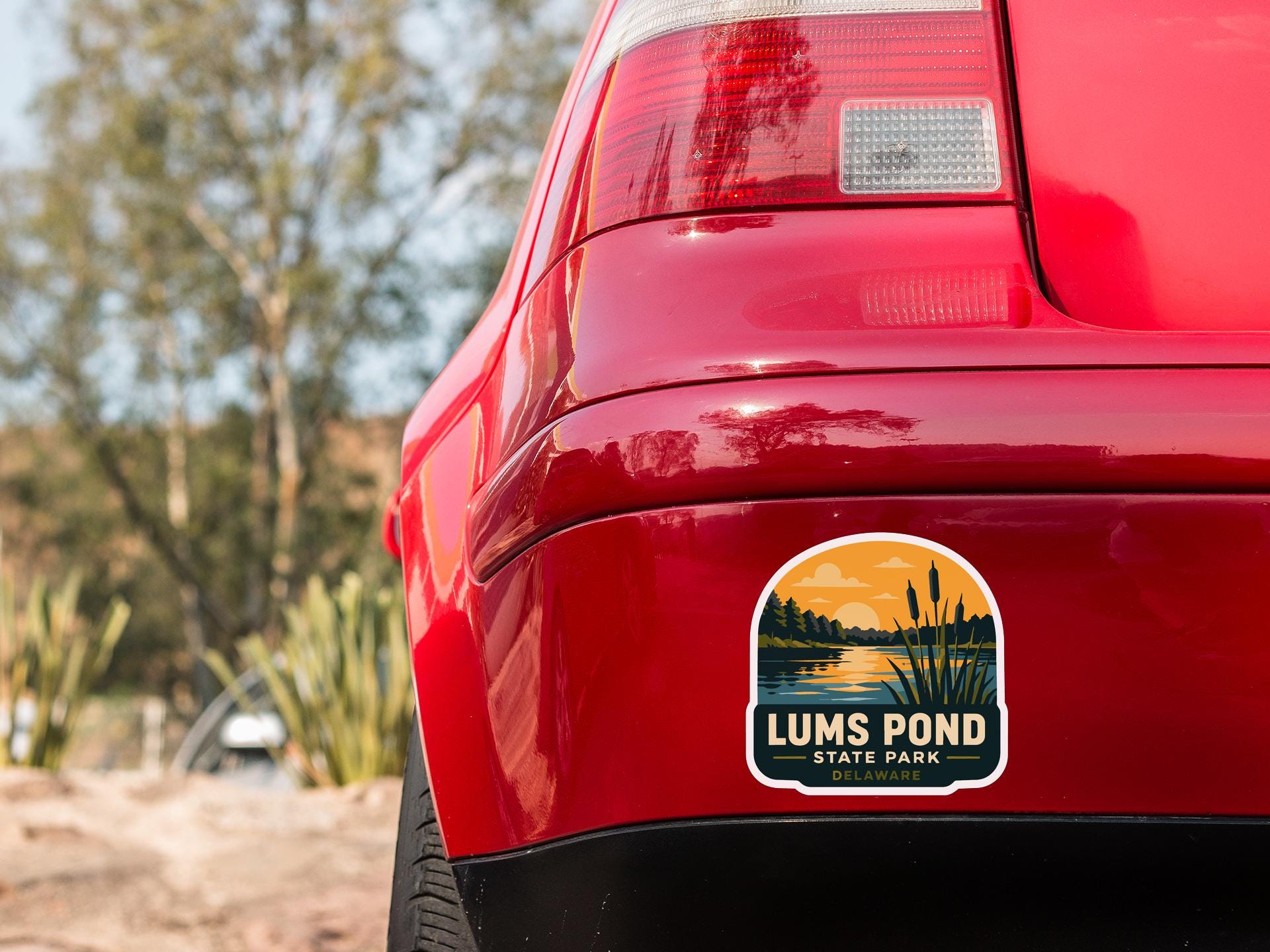 the rear end of a red car with a sticker on the trunk that says "LUMS POND STATE PARK".