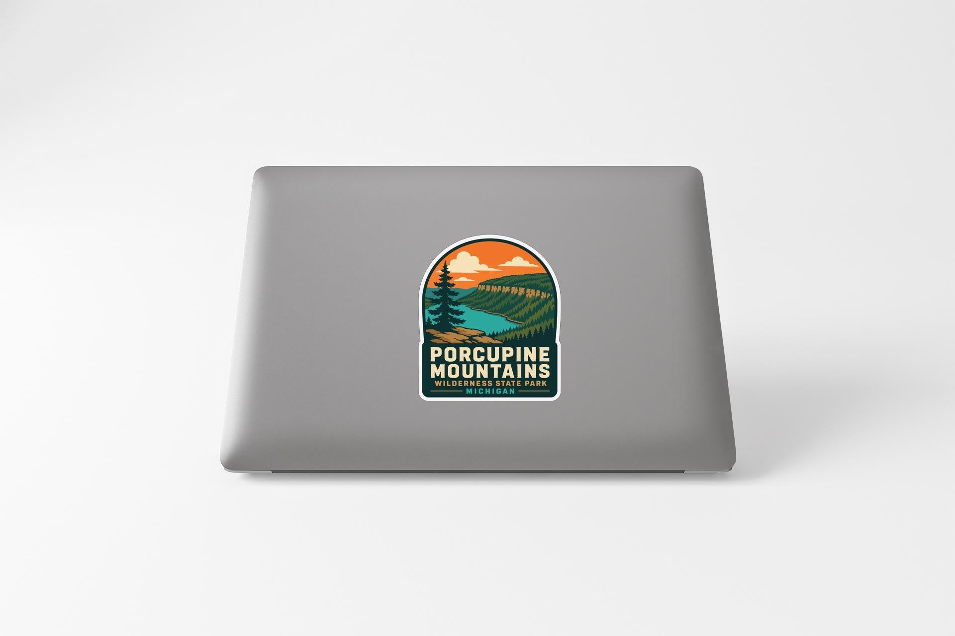A sticker on the back of a laptop, depicting a scenic mountain landscape with a lake and pine trees.