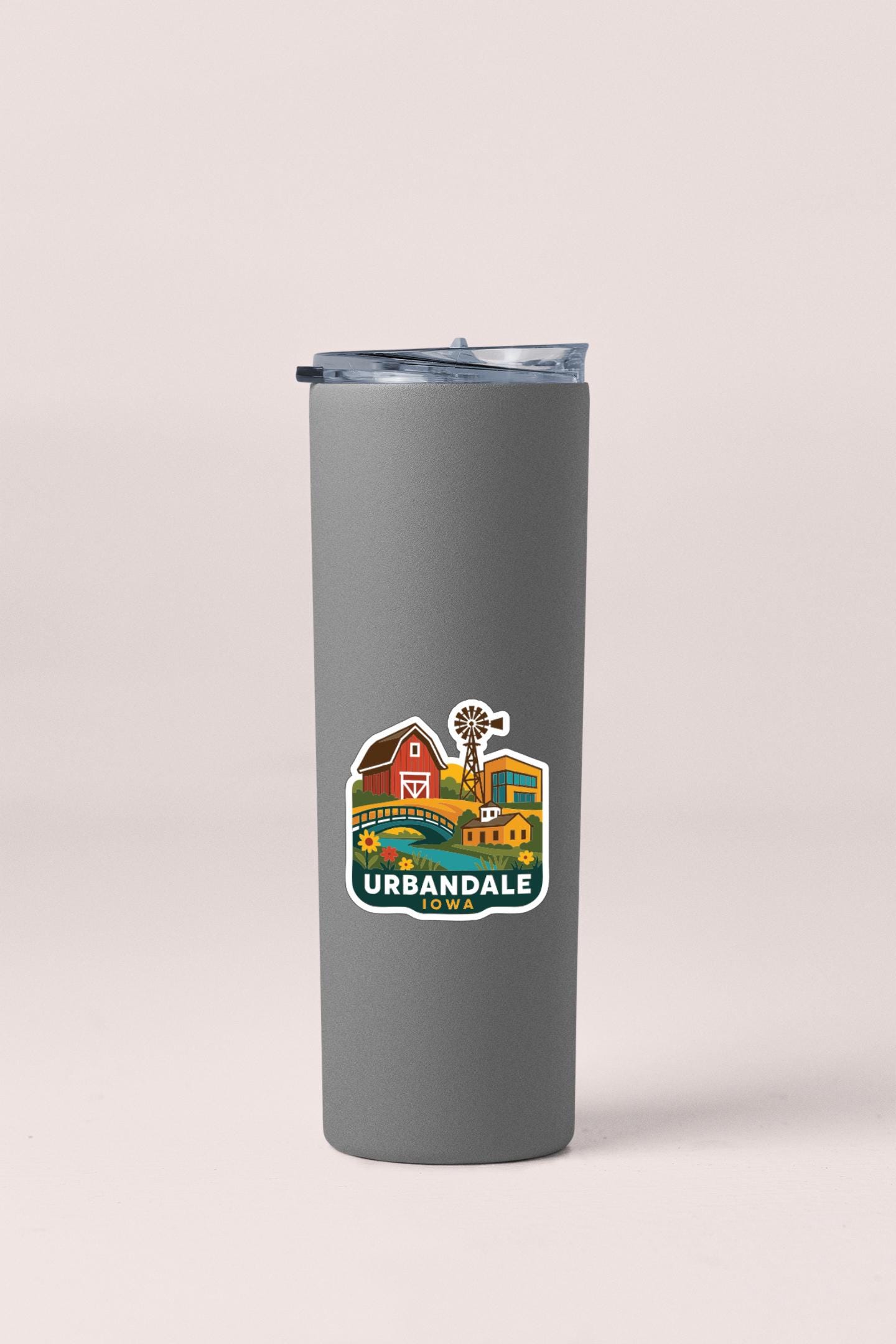 A gray insulated tumbler with a sticker depicting a rural scene in Urbandale, Iowa.