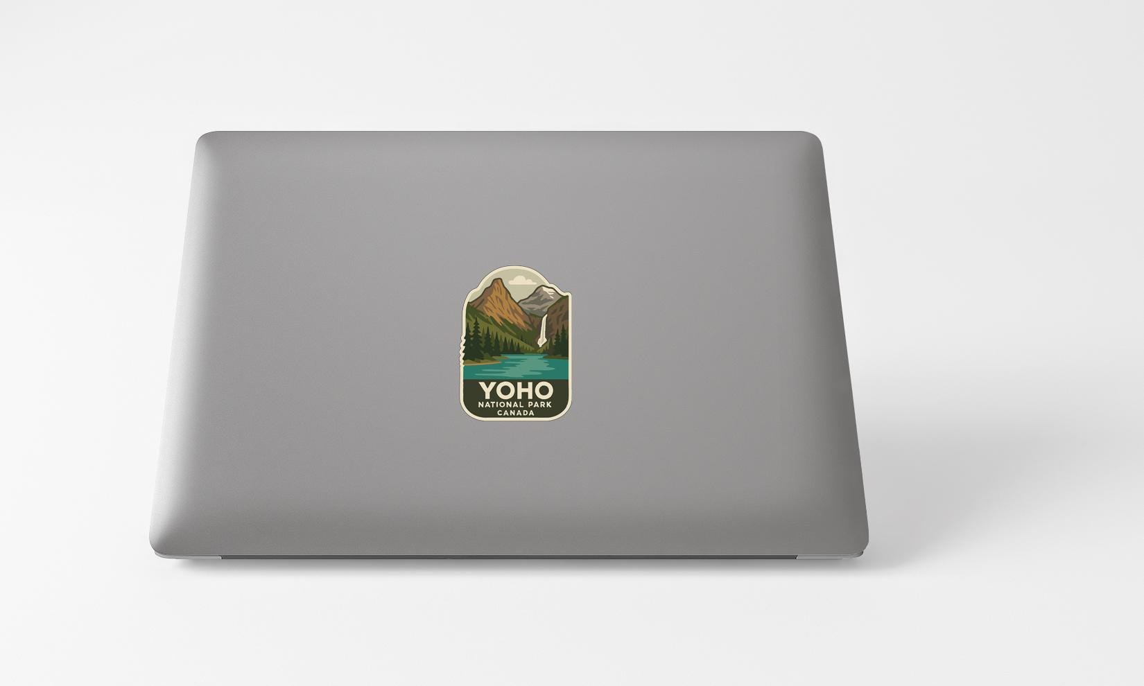 A sticker on the back of a laptop, depicting a scenic mountain landscape with a lake and a waterfall.