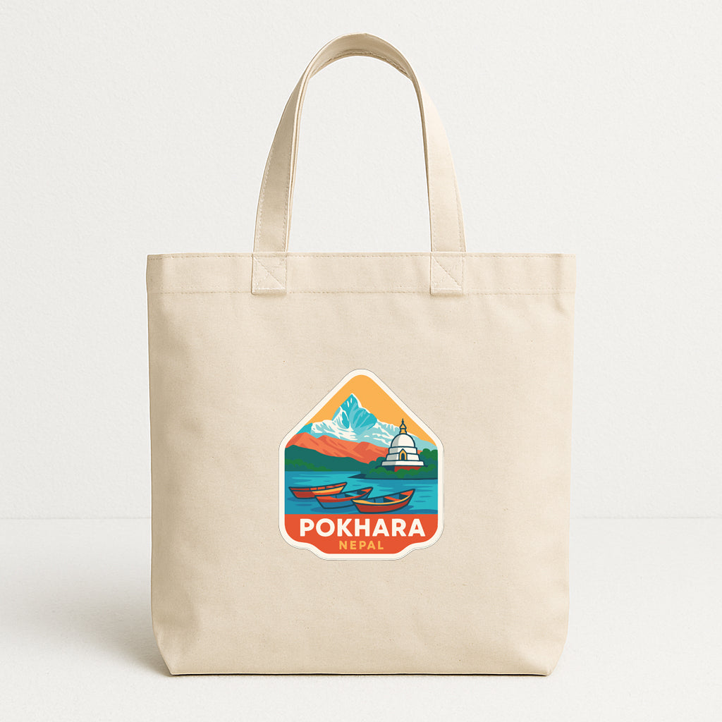A beige tote bag with a printed design depicting a scenic mountain landscape and a boat, along with the text "POKHARA NEPA".