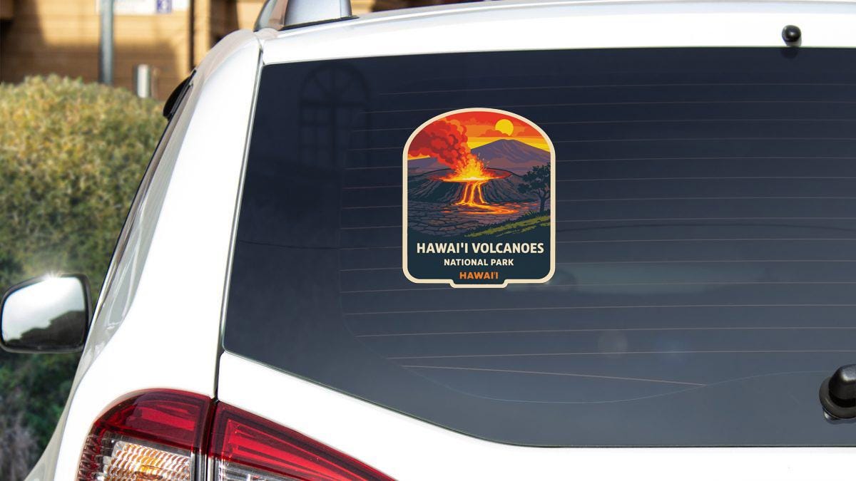 A sticker on the rear window of a car that says "HAWAII VOLCANOS NATIONAL PARK" with an illustration of a volcano and a sunset.
