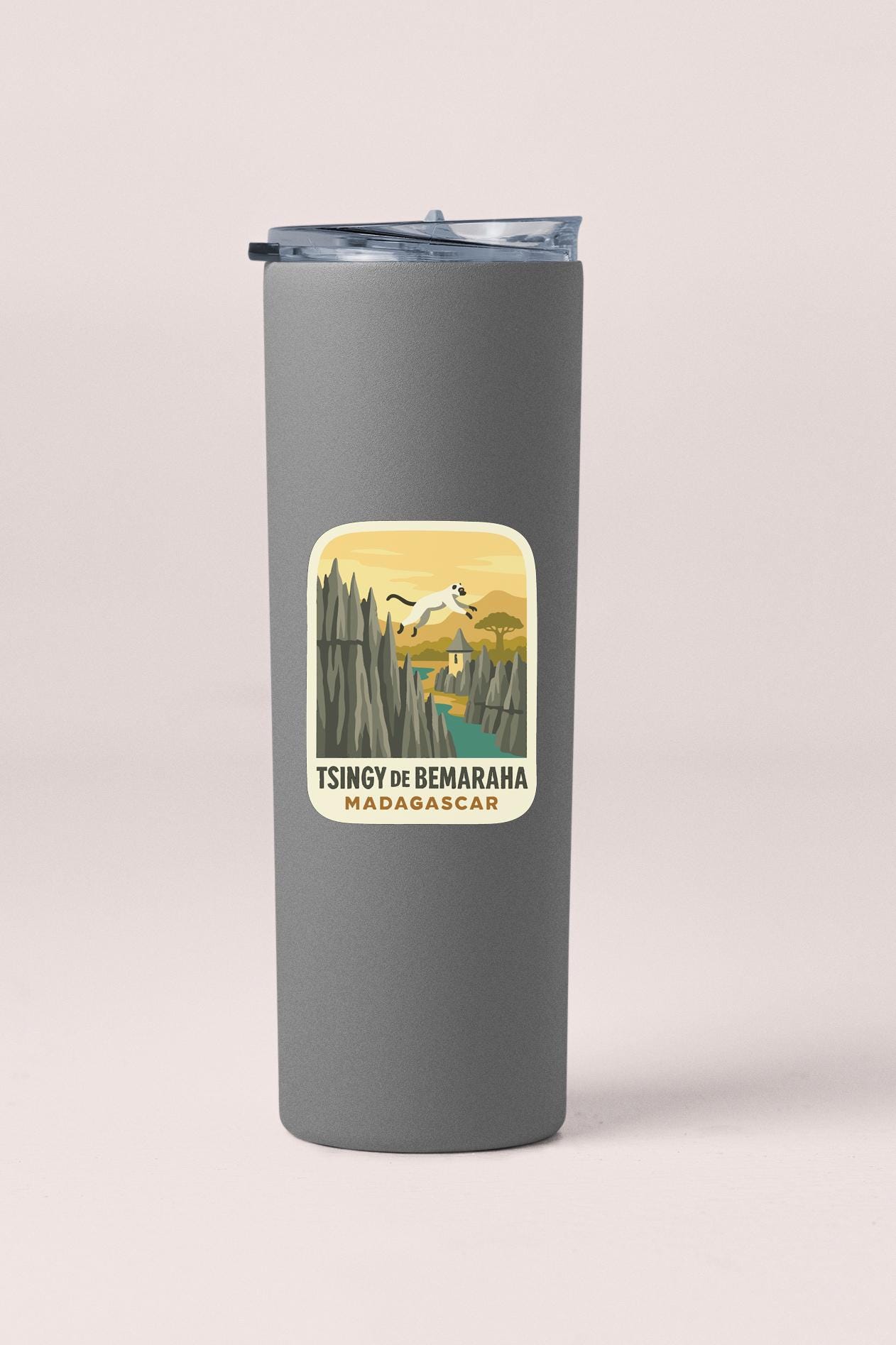 A gray tumbler with a sticker depicting a scenic landscape, including mountains, a river, and a bird in flight.