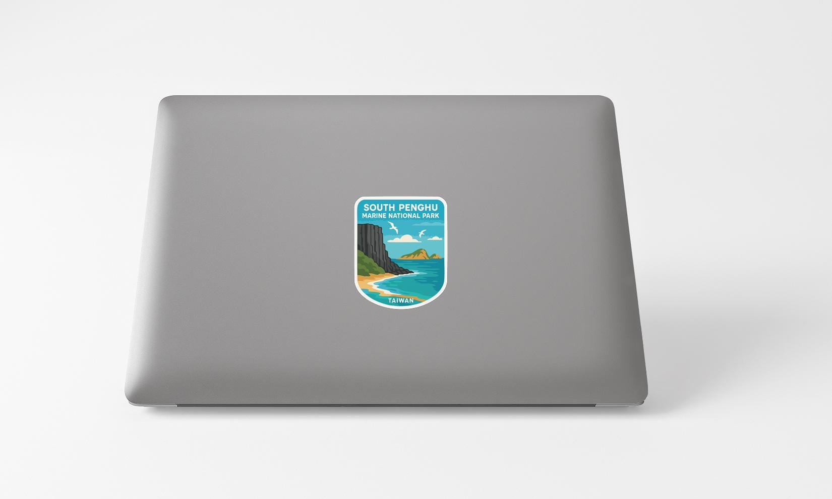 A sticker on the back of a laptop, depicting a scenic coastal landscape with mountains, water, and a beach.