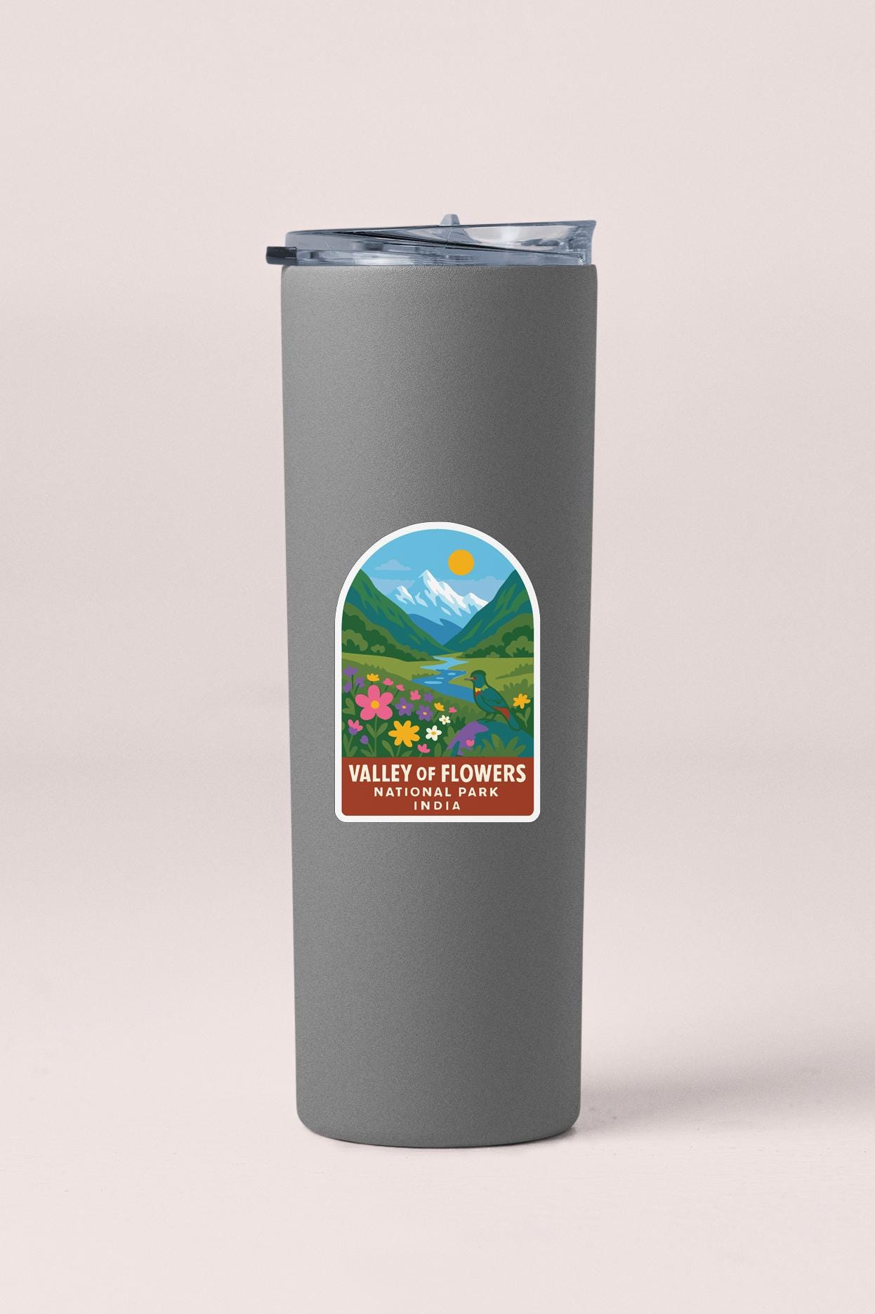 A gray insulated tumbler with a label that features a scenic landscape of mountains, flowers, and a sun.