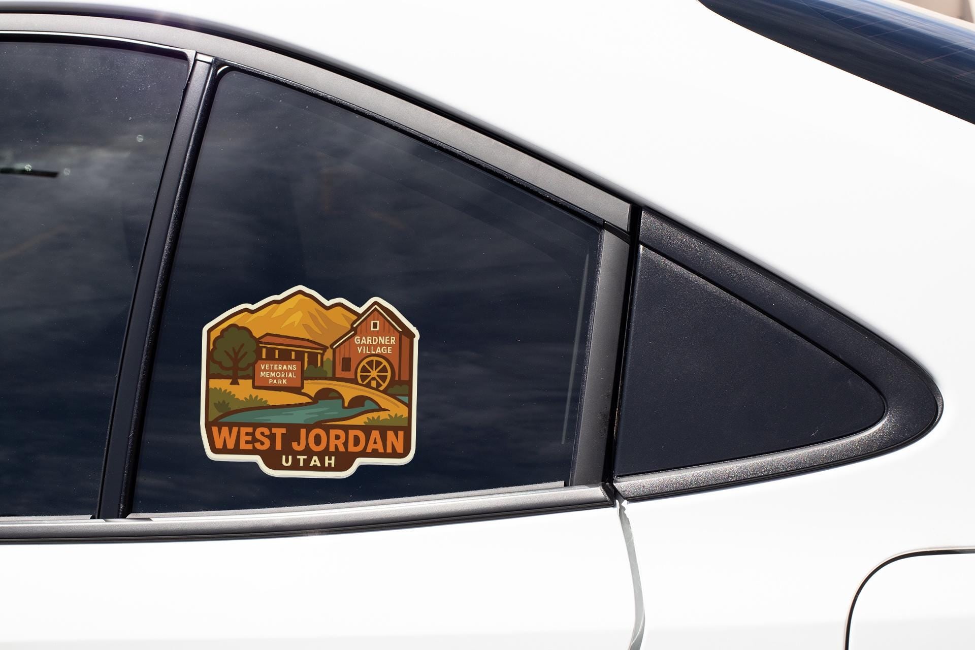 A sticker on the side of a car window, depicting a scenic landscape with mountains and a building, along with the text "WEST JORDAN UTAH".