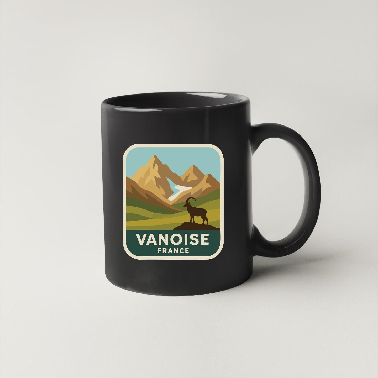A black coffee mug with a sticker depicting a mountain landscape and a goat.
