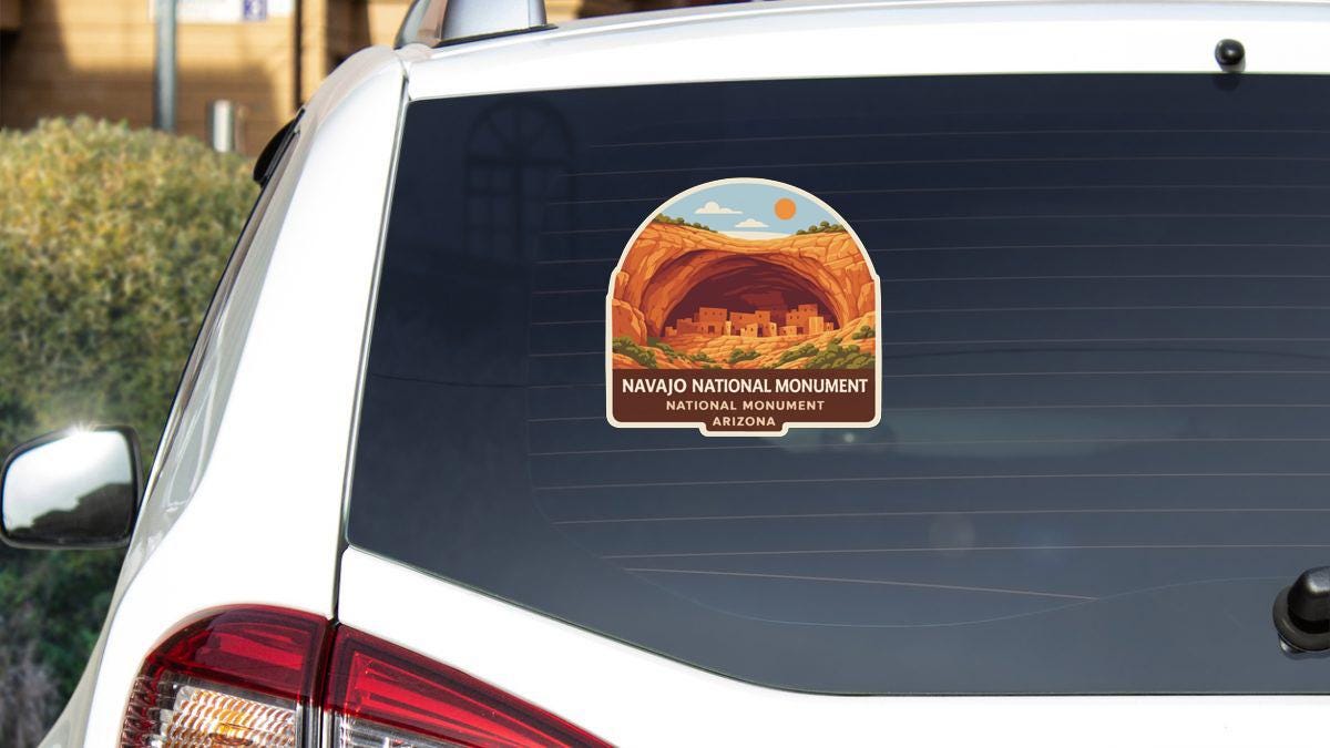 A sticker on the rear window of a white car, depicting the Navajo National Monument in Arizona.