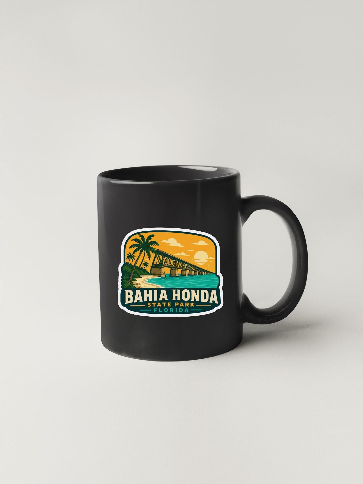 A black coffee mug with a sticker depicting a tropical beach scene and palm trees, along with the text "BAHIA HONDA FLORIDA".