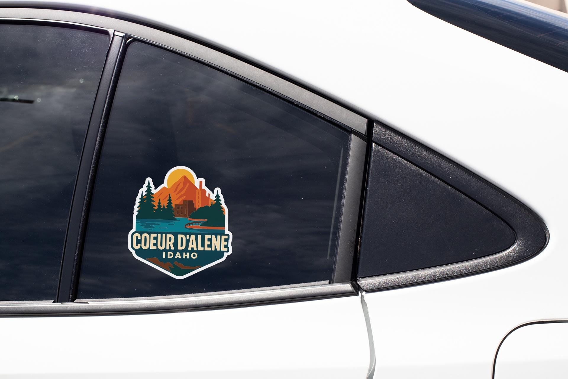 A sticker on the side of a car window, featuring a mountain landscape with a sunset.