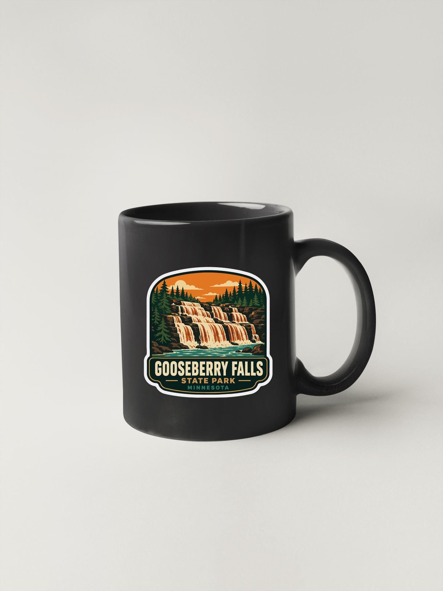 A black coffee mug with a graphic design depicting a waterfall and forest landscape, along with the text "GOOSEBERRY FALLS STATE PARK".