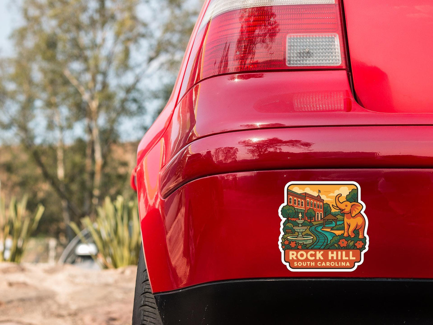 the rear end of a red car with a sticker on the trunk that features a scenic illustration of a landmark.