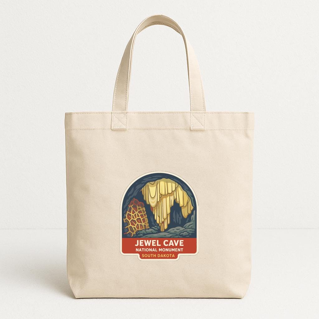 A beige tote bag with a graphic design featuring a cave and the text "JEWEL CAVE NATIONAL MONUMENT OF DALLAS" printed on it.